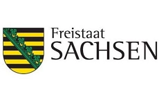 Zu sehen ist das Logo des deutschen Bundeslandes Sachsen. Links befindet sich ein Wappenschild mit waagerechten schwarzen und goldgelben Streifen. Diagonal von links oben nach rechts unten verläuft ein grüner Rautenkranz. Rechts neben dem Wappen steht in schwarzer Schrift der Text „Freistaat Sachsen“, wobei „Freistaat“ kleiner und „SACHSEN“ deutlich größer geschrieben ist. Der Hintergrund ist weiß.